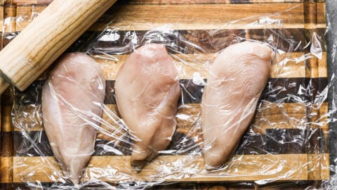 Raw chicken breasts in plastic wrap on a cutting board