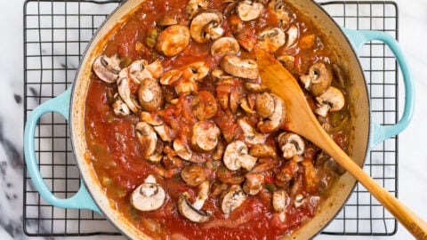 Mushrooms being added to a Dutch oven with red sauce