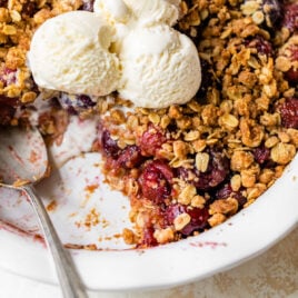 homemade sweet cherry crisp with a serving removed and topped with three scoops of vanilla ice cream
