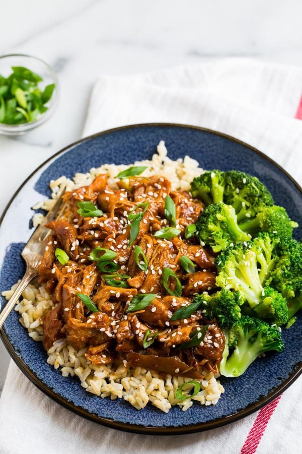 shredded chicken thighs in a brown asian sauce served on a plate with rice and broccoli