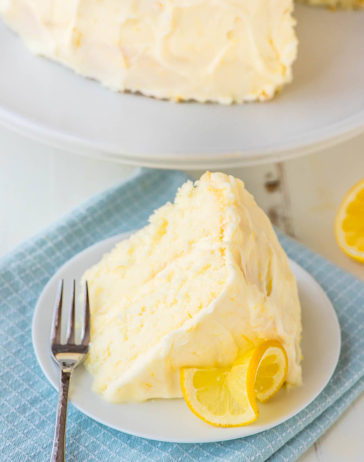 Slice of lemon layer cake with lemon cream cheese frosting on a white dessert plate