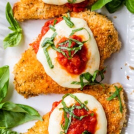 crispy and healthy oven baked chicken parmesan on a plate with mozzarella, tomato sauce, and basil