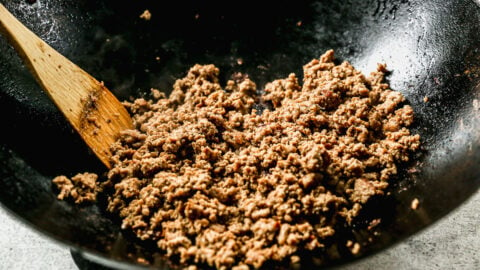 a wok of ground turkey being stirred by a wooden spoon