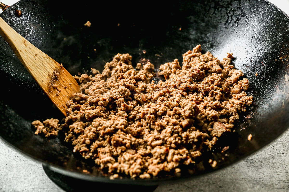 a wok of ground turkey being stirred by a wooden spoon