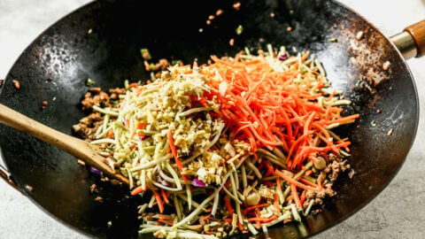 adding grated carrots and broccoli slaw to a wok of seasoned ground turkey and vegetables
