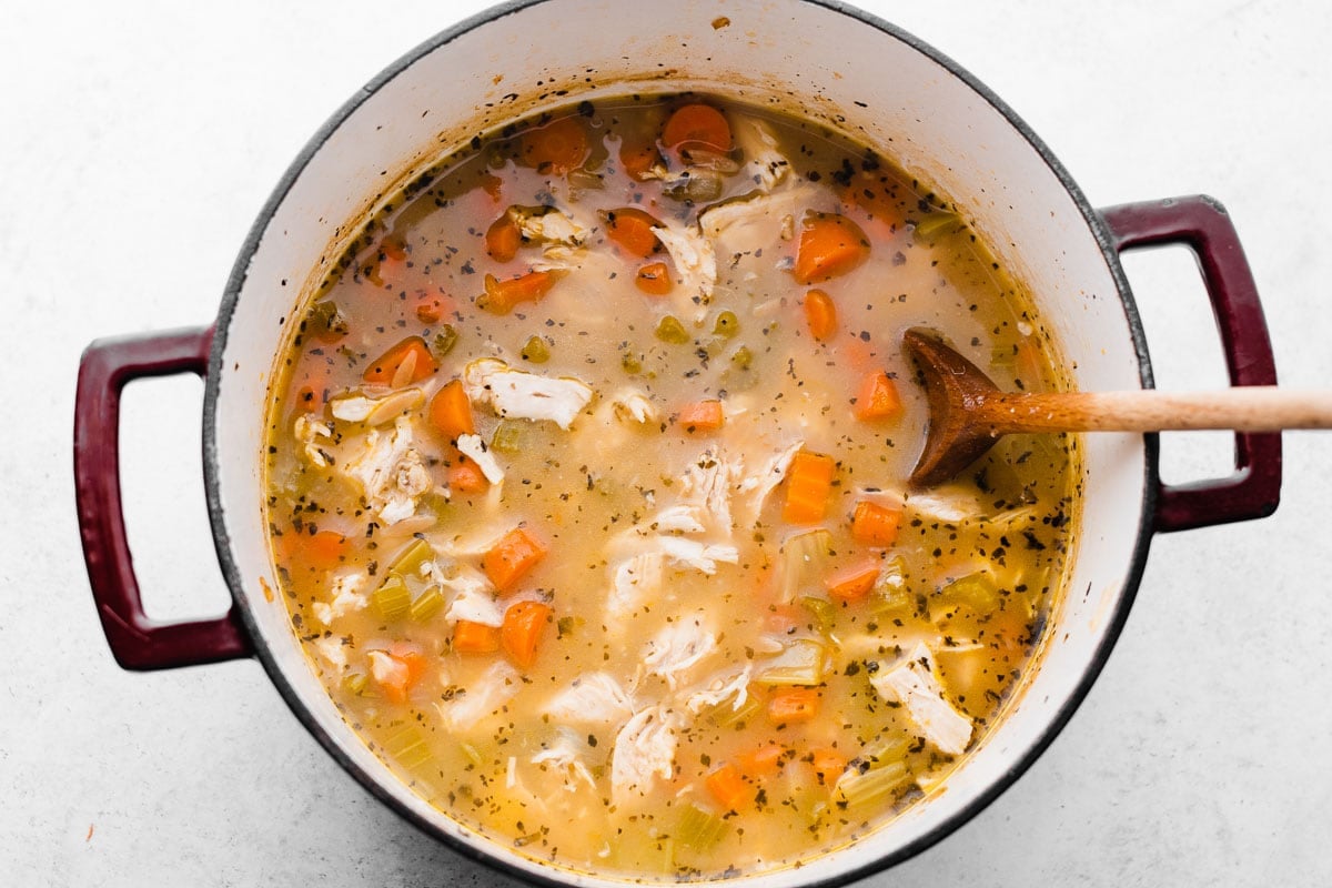 shredded chicken in a pot of steaming broth with vegetables