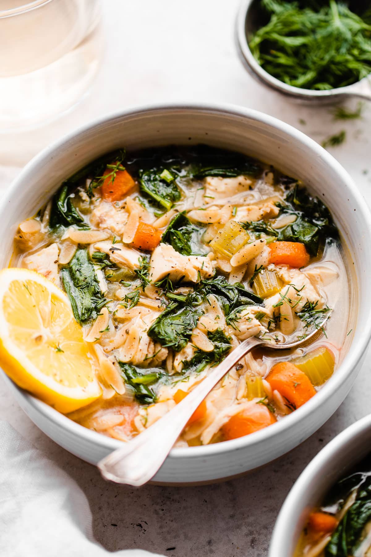 A white bowl with chicken soup with orzo and lemon