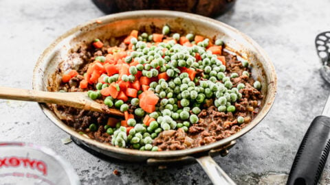 Frozen peas and carrots being stirred into a skillet