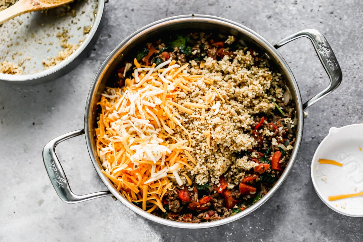 Cheese and quinoa being added to a skillet of ground beef and vegetables for stuffed peppers