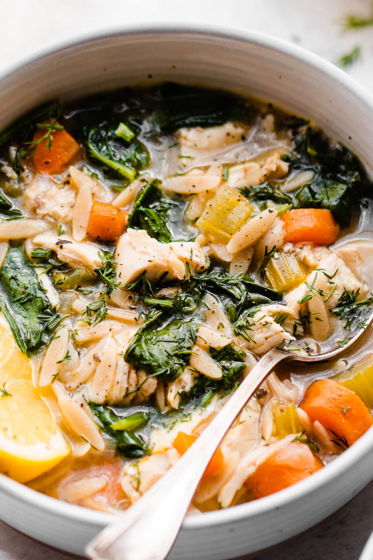 A bowl of healthy lemon chicken orzo soup with spinach