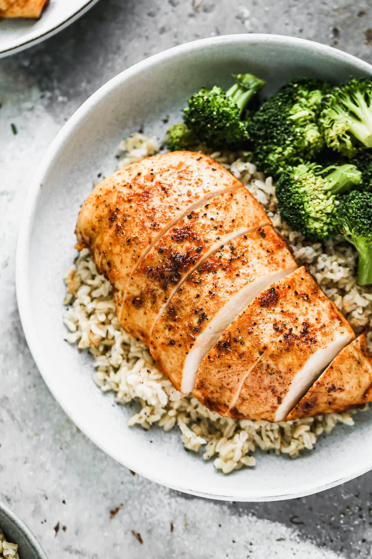 A chicken breast served on a bowl of rice and broccoli