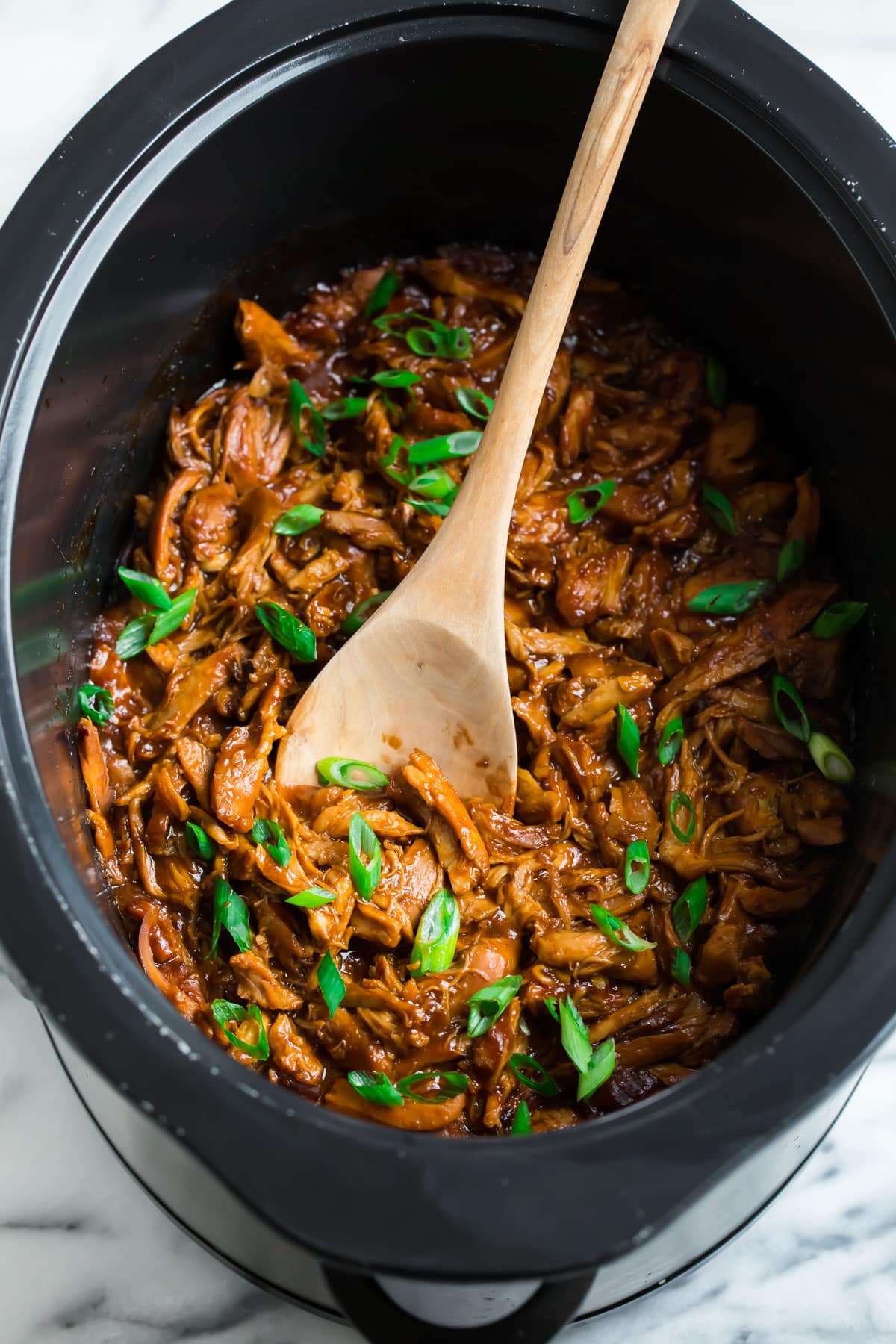 Easy slow cooker chicken in a crockpot with a wooden spoon
