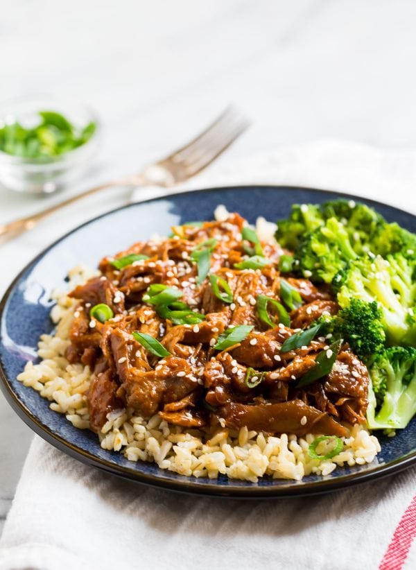Shredded chicken in a sauce served on a plate with rice and broccoli