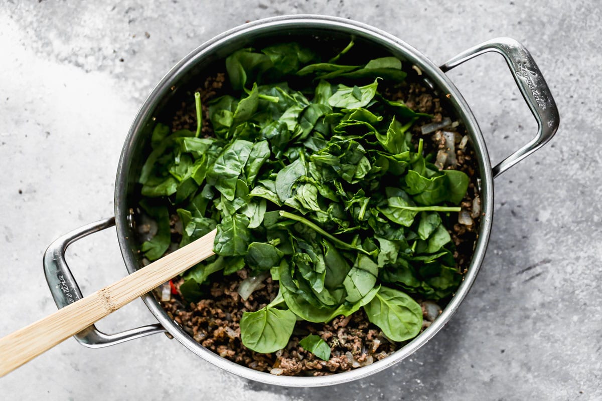 Spinach being added to a skillet of ground beef